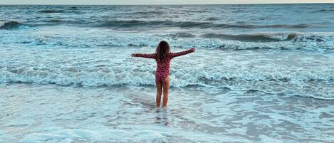 Escena de playa con una persona de pie en el agua.