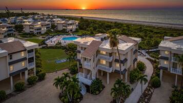 A resort with multiple buildings, a swimming pool, and a view of the ocean at sunset.