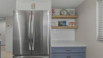 A kitchen with a stainless steel refrigerator, a blue cabinet, and a clock on the wall.