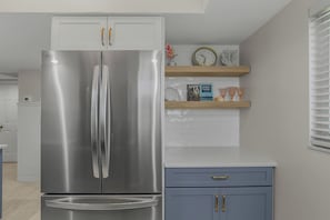 Una cocina con un refrigerador de acero inoxidable, un armario azul y un reloj en la pared.
