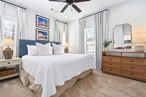 A bedroom with a large bed, a wooden dresser, a ceiling fan, and two windows with curtains. - Lonestar on the Plains  Designer 3BR Cottage Pet Friendly Close to Campus (Auburn)
