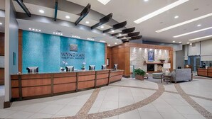 A reception area with a blue textured wall, a wooden reception desk, and a seating area with a fireplace. - Heart of National harbor (Austin)
