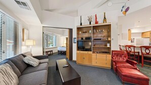 Ein modernes Wohnzimmer mit einer Couch, einem Couchtisch, einem Fernseher und einem roten Ledersessel. Es gibt ein Holzregal und einen Essbereich mit Tisch und Stühlen.