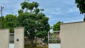 A gated entrance with a concrete wall, a metal gate, and a tree in the background. - Casa Novo Airão Espaço com dois chalés (Novo Airão)