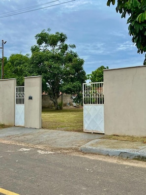A gated entrance with a concrete wall, a metal gate, and a tree in the background. - Casa Novo Airão Espaço com dois chalés (Novo Airão)