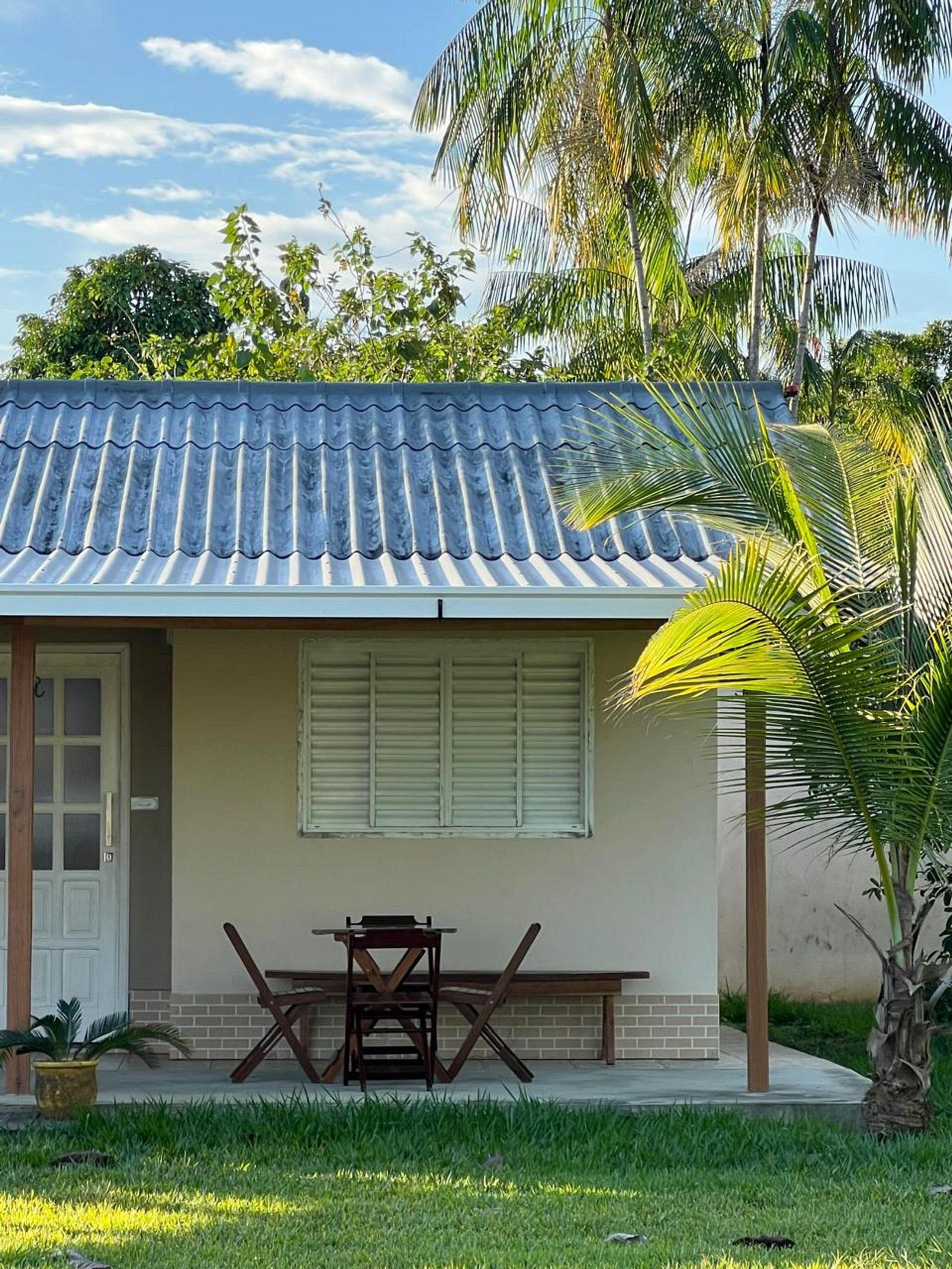 A small house with a tiled roof, a door, a window with shutters, and a table with chairs outside.