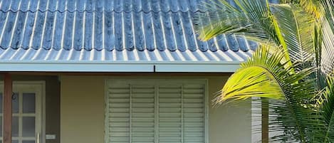Uma pequena casa com telhado de telhas, porta, janela com persianas e uma mesa com cadeiras do lado de fora.