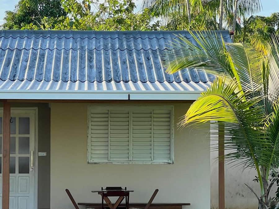 A small house with a tiled roof, a door, a window with shutters, and a table with chairs outside.