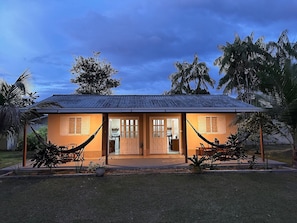 A two-story building with a tiled roof, a front porch, and a hammock. - Casa Novo Airão Espaço com dois chalés (Novo Airão)