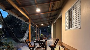 A covered patio with a table and chairs, a hammock, and a view of the outdoors. - Casa Novo Airão Espaço com dois chalés (Novo Airão)