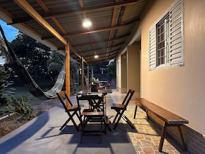 A covered patio with a table and chairs, a hammock, and a view of the outdoors. - Casa Novo Airão Espaço com dois chalés (Novo Airão)