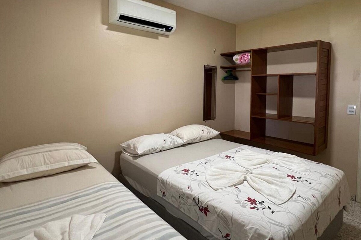 A hotel room with two beds, an air conditioning unit, a mirror, and a wooden shelf.