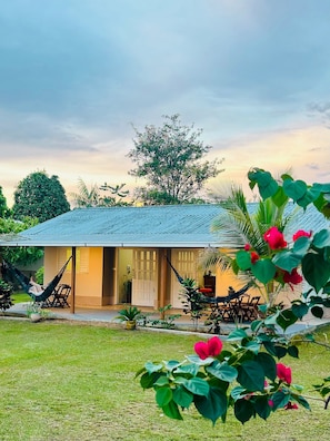 A house with a tiled roof, a hammock, and a garden with red flowers. - Casa Novo Airão Espaço com dois chalés (Novo Airão)