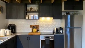 A modern kitchen with dark cabinets, a stainless steel refrigerator, a built-in oven, and a coffee maker on the counter. - Highlander - Dinner Plain (Dinner Plain)