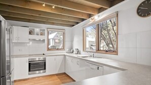 A modern kitchen with white cabinetry, stainless steel appliances, and a large window providing natural light. - Frankies - Dinner Plain (Dinner Plain)