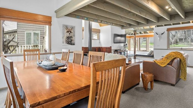 A spacious living area with a wooden dining table, comfortable seating, and large windows offering views of the outdoors. - Frankies - Dinner Plain (Dinner Plain)
