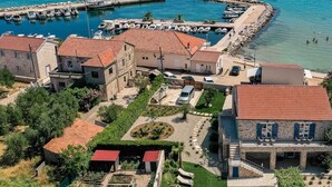 Vista aérea de un pueblo costero con edificios de piedra tradicionales, un puerto deportivo con barcos y un mar azul cristalino.