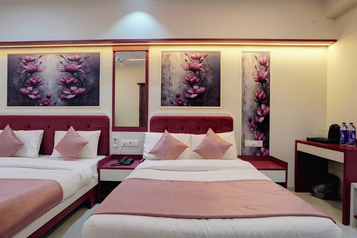Habitación de hotel con dos camas, una mesita de noche con teléfono, un espejo y cuadros con motivos florales en las paredes.