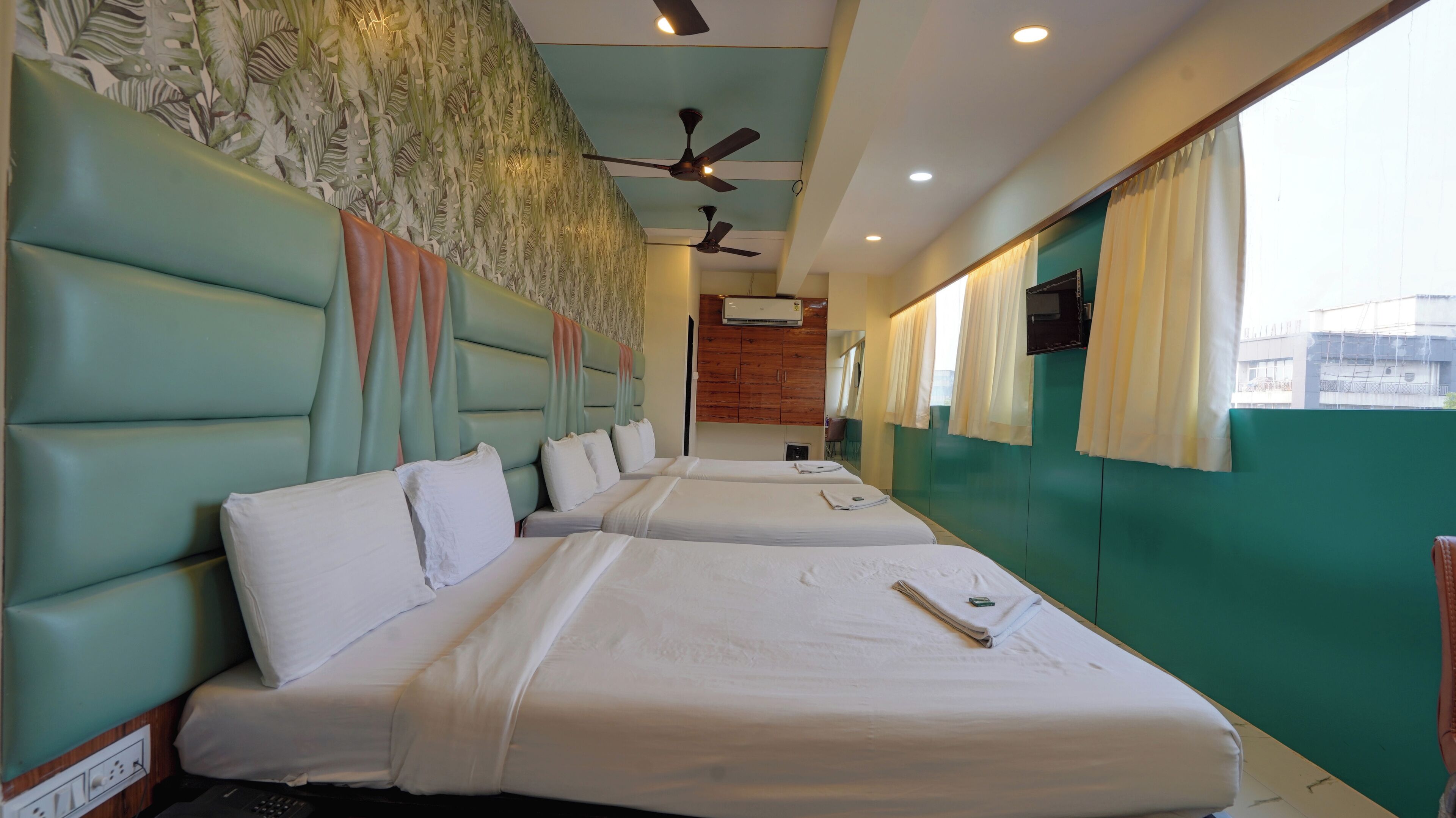 Habitación de hotel con dos camas, ventilador de techo, aire acondicionado y vista al exterior por la ventana.