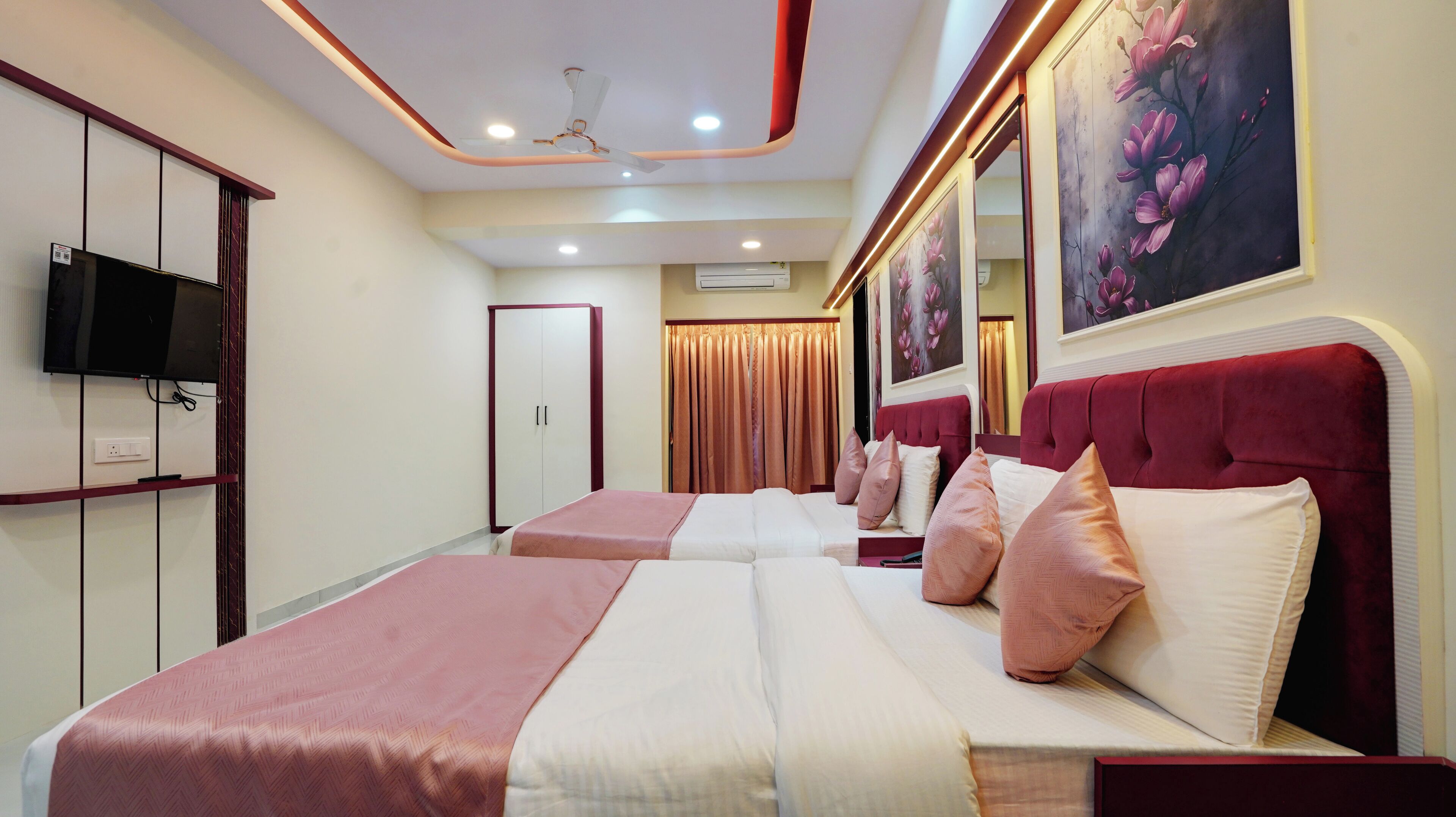 A hotel room with two beds, a TV, a wardrobe, and a ceiling fan.
