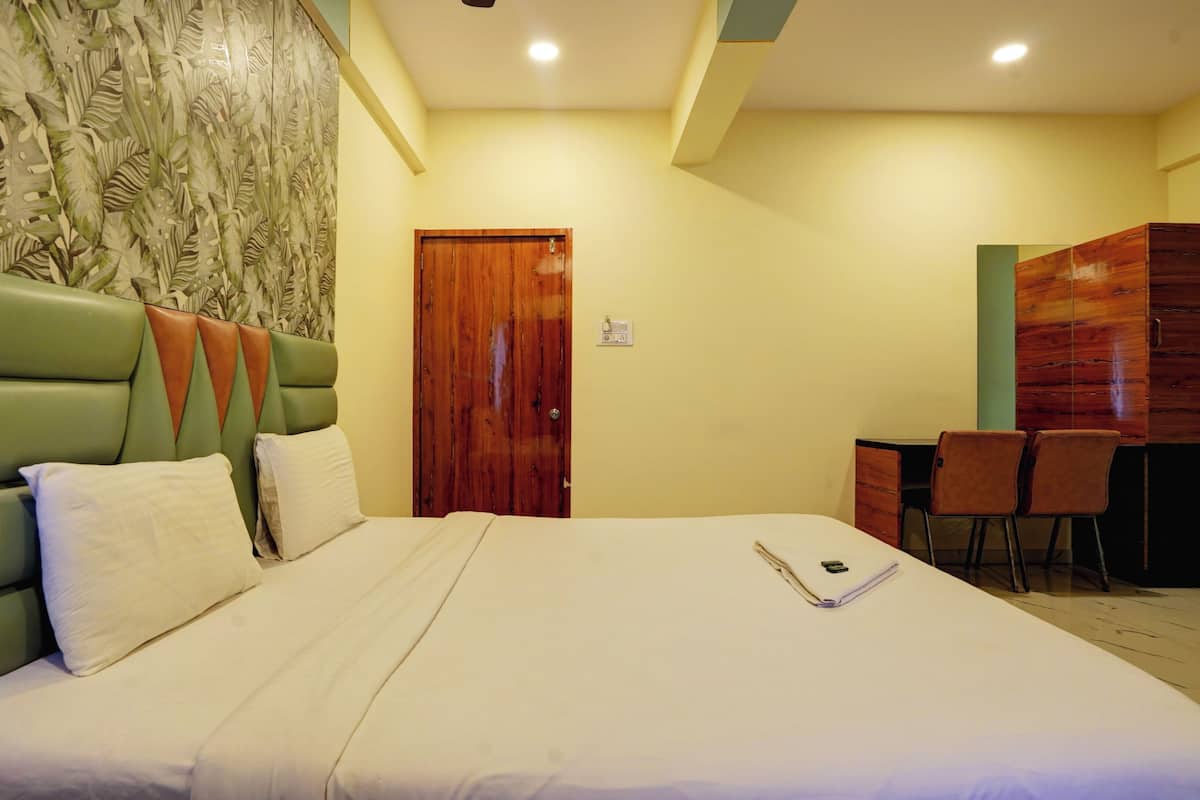 Habitación de hotel con una cama grande, una puerta de madera, un escritorio pequeño con sillas y una pared con un diseño de hojas.