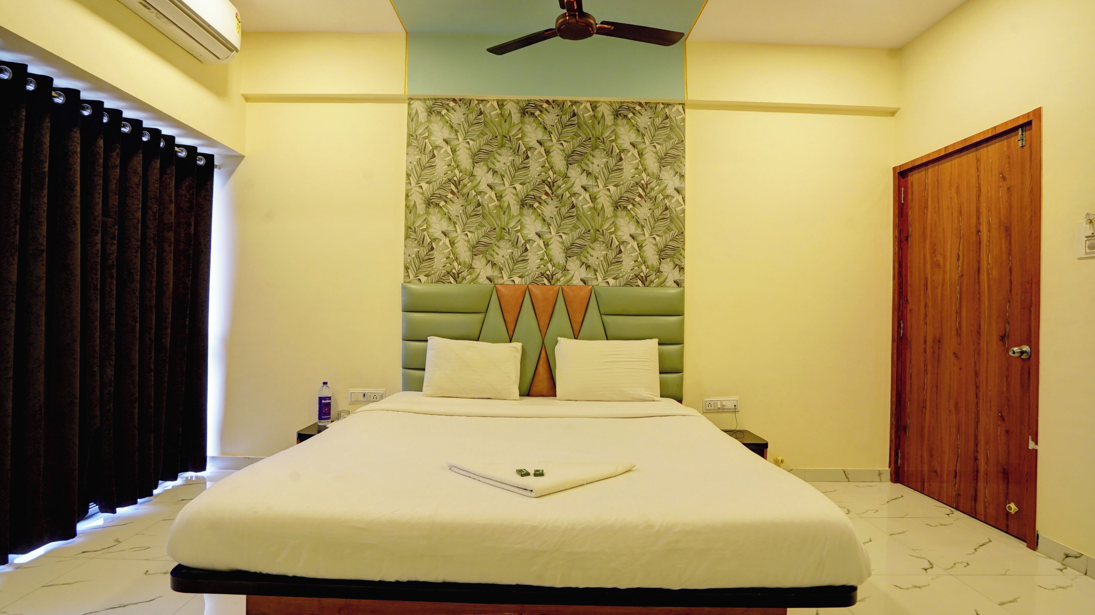 A neatly made bed with a white comforter and pillows, a green upholstered headboard, and a wooden door to the right.