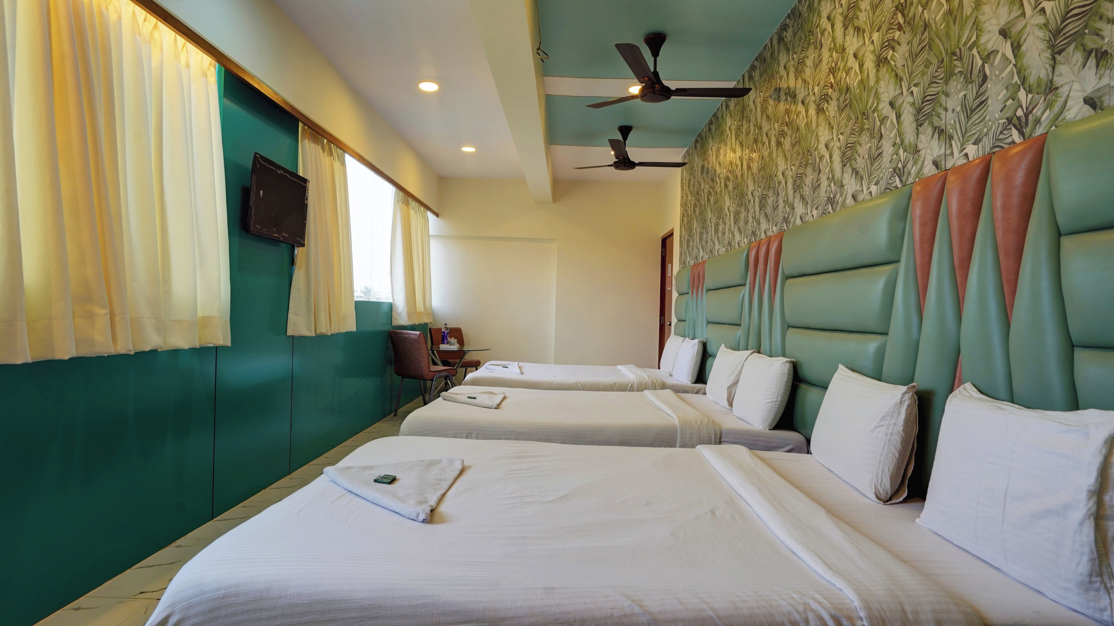A hotel room with two beds, a desk, a chair, a ceiling fan, and a wall with a leaf pattern.