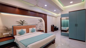 A modern bedroom with a curved headboard, a large bed with a blue bedspread, a nightstand, a bedside table with a lamp, and a wardrobe. - Hotel Balaji Residency Dombivli (Kalyan)