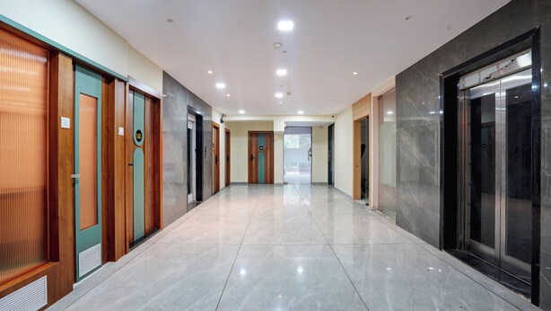 A modern hallway with a marble floor, wooden and glass doors, and an elevator. - Hotel Balaji Residency Dombivli (Kalyan)