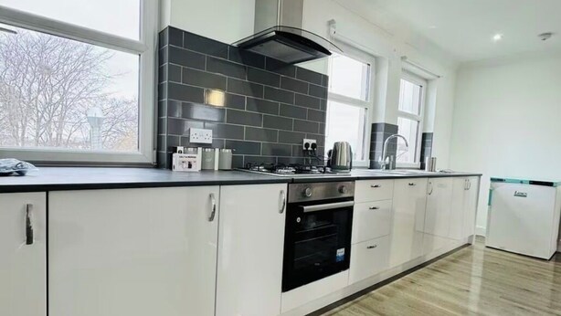 Una cucina moderna con mobili bianchi, una parete di fondo rivestita in piastrelle nere, una cappa aspirante in acciaio inossidabile e un forno integrato.