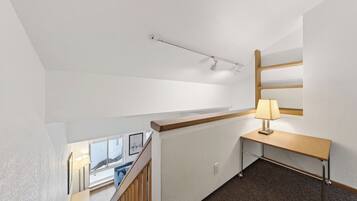 A hotel room with a desk, lamp, and a view of the outside through a window.