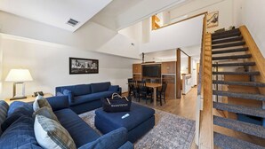 A living room with a blue sofa, a coffee table, and a TV. There is a staircase leading to another level. - The Traverse by Avantstay Ski-in/ski-out Condo Pool, Hot Tub Access Steps to Kt-22 (Olympic Valley)