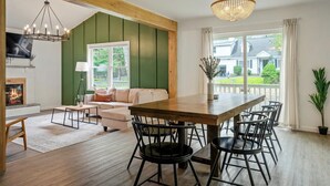 A spacious living room with a wooden dining table, black chairs, a beige sofa, and a fireplace. - Hot Tub + Sauna Escape | Game Room, Fire Pit, Sleeps 14 (Tobyhanna)