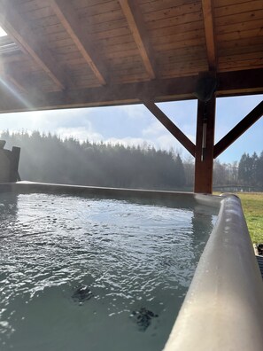 Un bain à remous sous un toit en bois, avec vue sur une zone boisée.