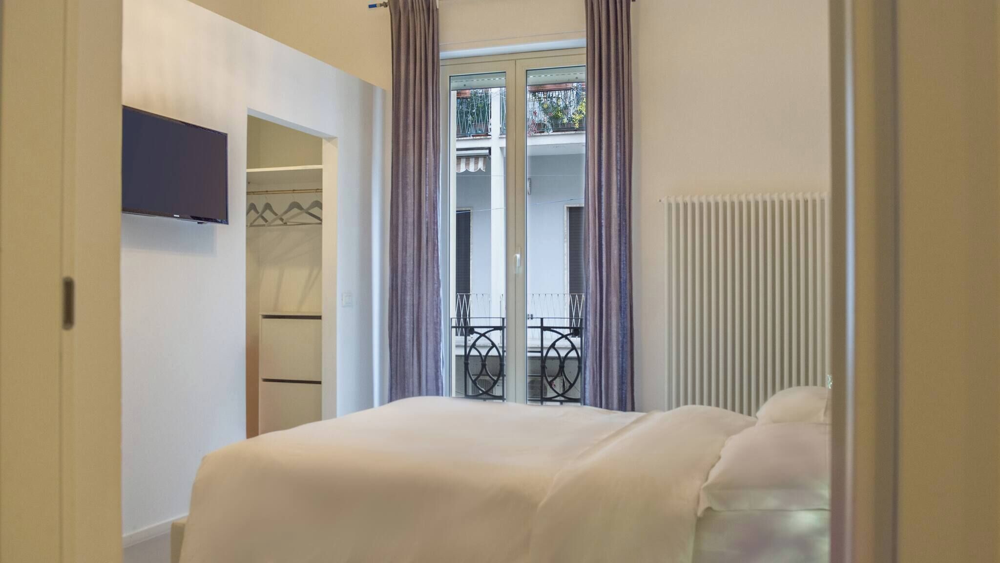 Una camera da letto con un letto, un armadio, una TV e un balcone con ringhiera.