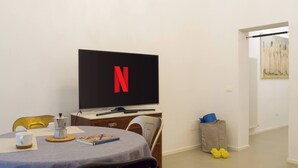 Ein Zimmer mit Fernseher, der das Netflix-Logo zeigt, einem Esstisch mit einem Buch und einer Mülltonne.