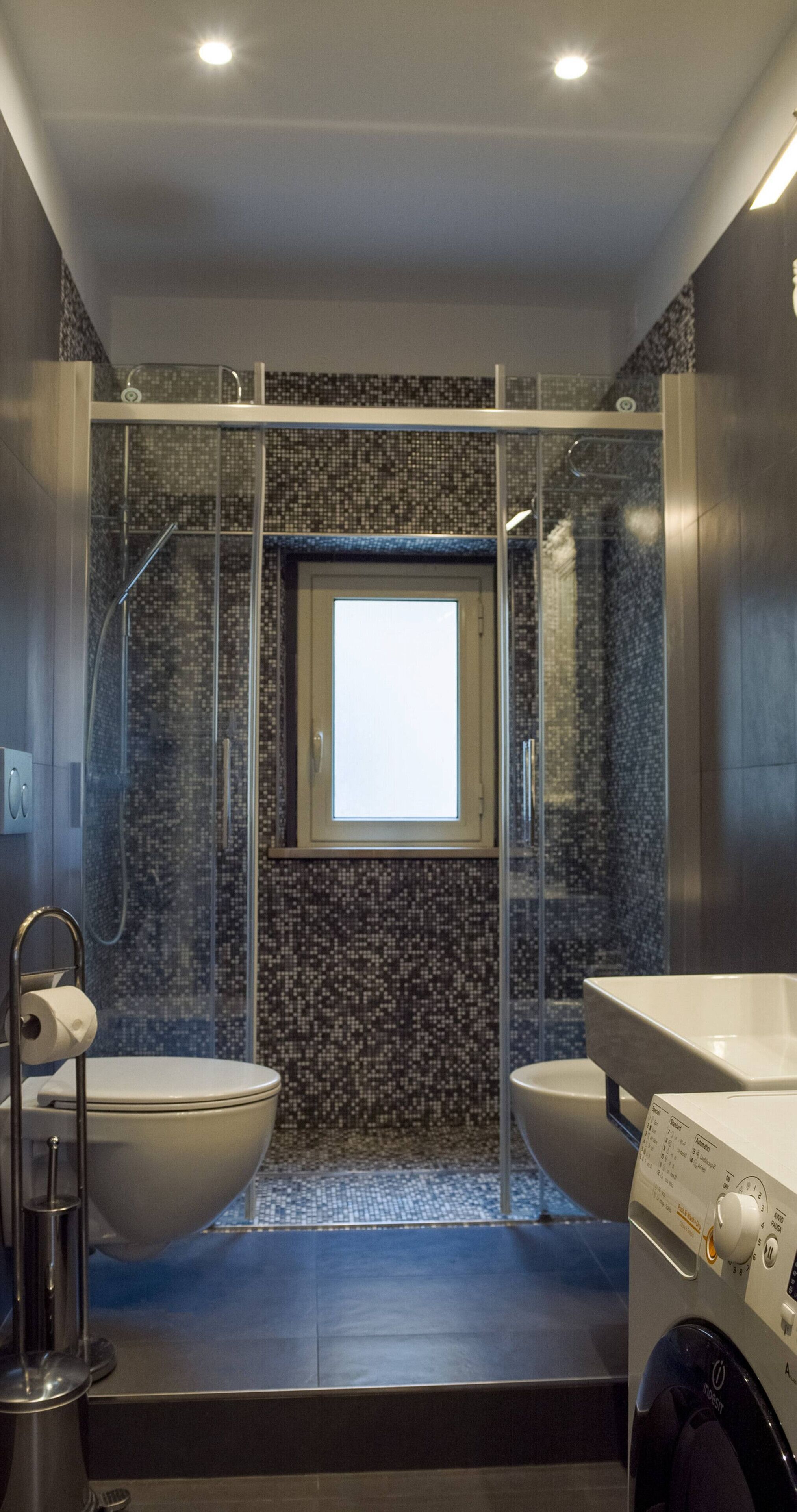 A modern bathroom with a glass-enclosed shower, a toilet, and a washing machine.