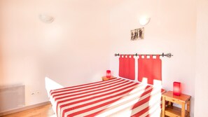Une chambre à coucher avec un lit, une table de chevet, une couvre-lit à rayures rouges, un rideau rouge, un tableau accroché au mur et une lampe rouge.