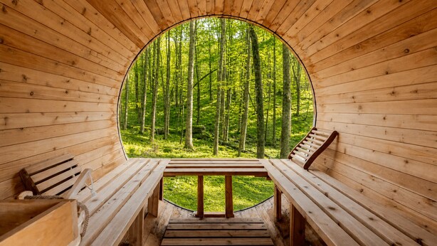 Una cabaña de madera con un ventanal circular, bancos de madera y vistas a un bosque.