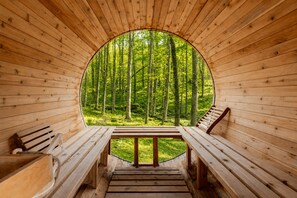 A wooden cabin with a circular window, wooden benches, and a view of a forest. - 8BR Spa Lodge • Hot Tub, Sauna, Steam Room (East Stroudsburg)