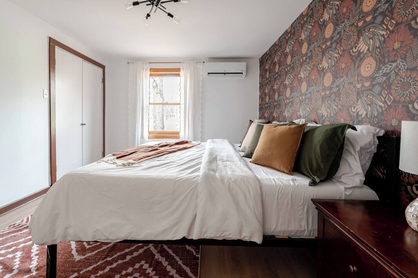 Un dormitorio con cama, ventana con cortinas, pared con diseño y lámpara de techo.