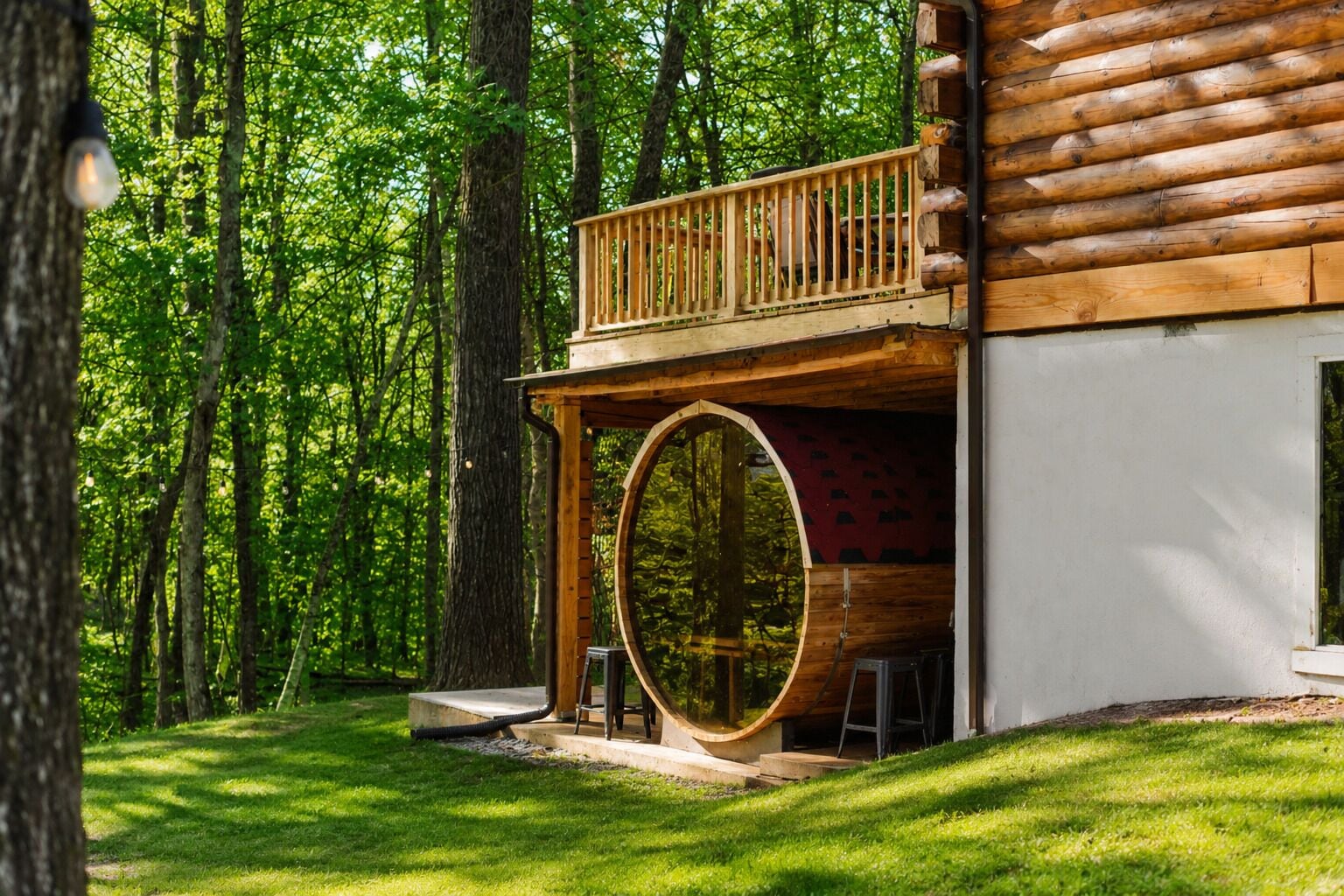 A log cabin with a wooden deck, a large circular window, and a forested backdrop.