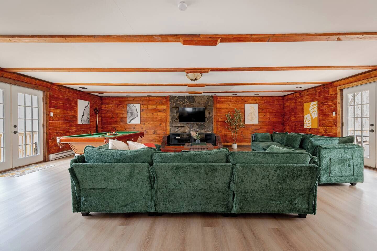 A spacious living room with a green sectional sofa, a pool table, and a stone fireplace.