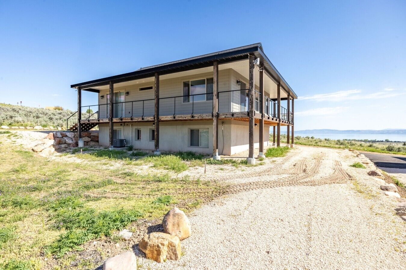 A two-story building with a balcony on the upper floor, a gravel driveway, and a hilly landscape in the background.