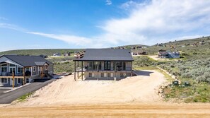 Ein modernes Haus mit überdachter Veranda, einer Auffahrt und einer hügeligen Landschaft im Hintergrund.