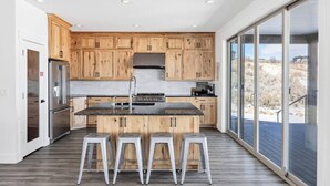 A modern kitchen with wooden cabinets, stainless steel appliances, and a large island with bar stools. - The Lazy Days Getaway at Bear Lake with Ideal Beach Access (Garden City)