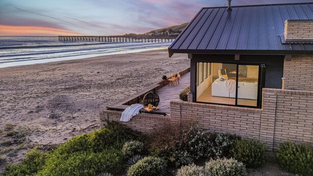 A beachfront property with a patio overlooking the beach, a brick exterior, and a large window. - The Jamie by Avantstay Oceanfront Stay + Firepit + Chef's Kitchen + Near Morro Bay (Cayucos)