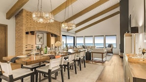 A dining area with a brick wall, wooden ceiling beams, and large windows overlooking the ocean. - The Jamie by Avantstay Oceanfront Stay + Firepit + Chef's Kitchen + Near Morro Bay (Cayucos)