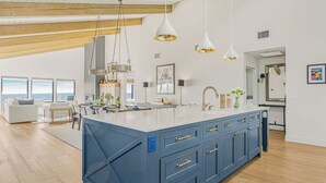 A spacious kitchen with a large island, pendant lighting, and a view of the ocean. - The Jamie by Avantstay Oceanfront Stay + Firepit + Chef's Kitchen + Near Morro Bay (Cayucos)