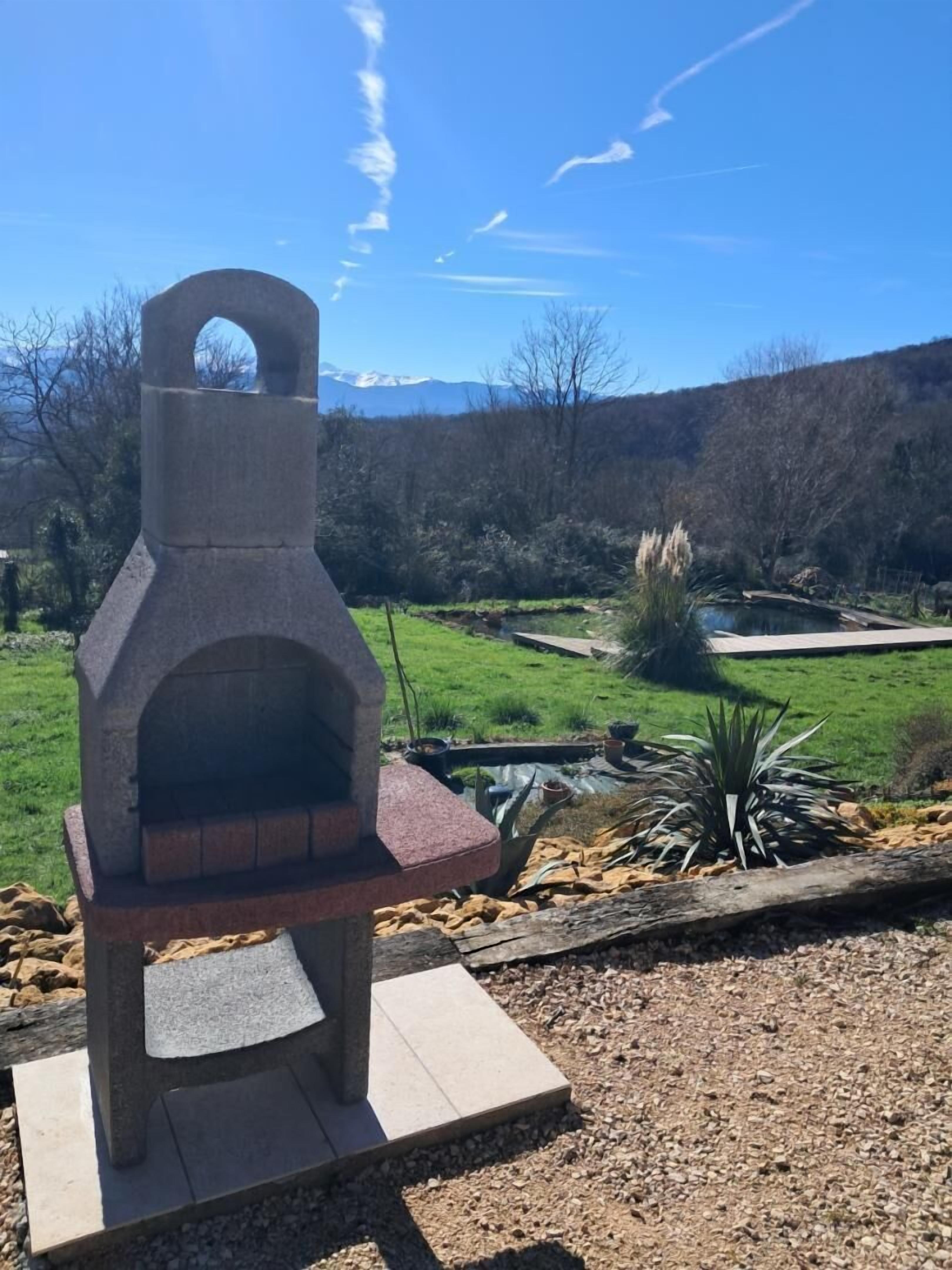 A stone outdoor oven in a garden with a view of mountains and a pond.